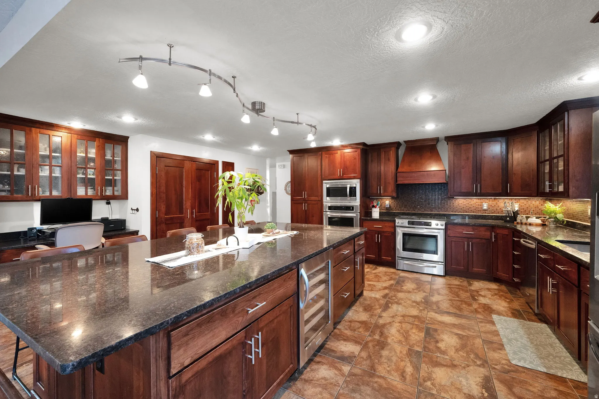 Kitchen with glass insert cabinets, dark stone counters, appliances with stainless steel finishes, a center island, and premium range hood