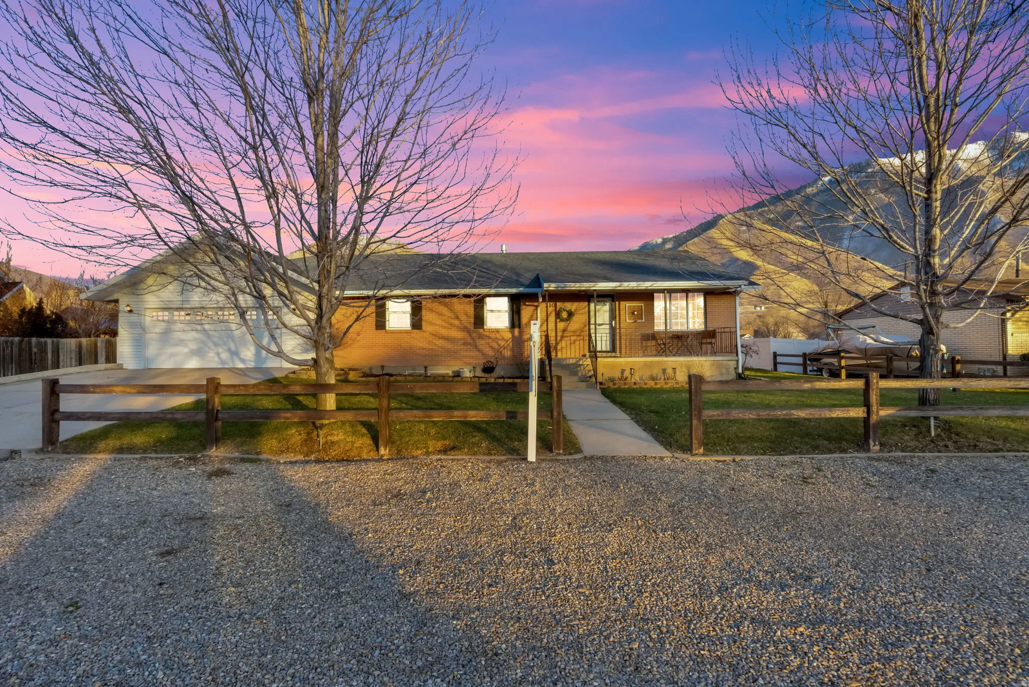 Single story home featuring driveway, a fenced front yard, covered porch, brick siding, and a garage
