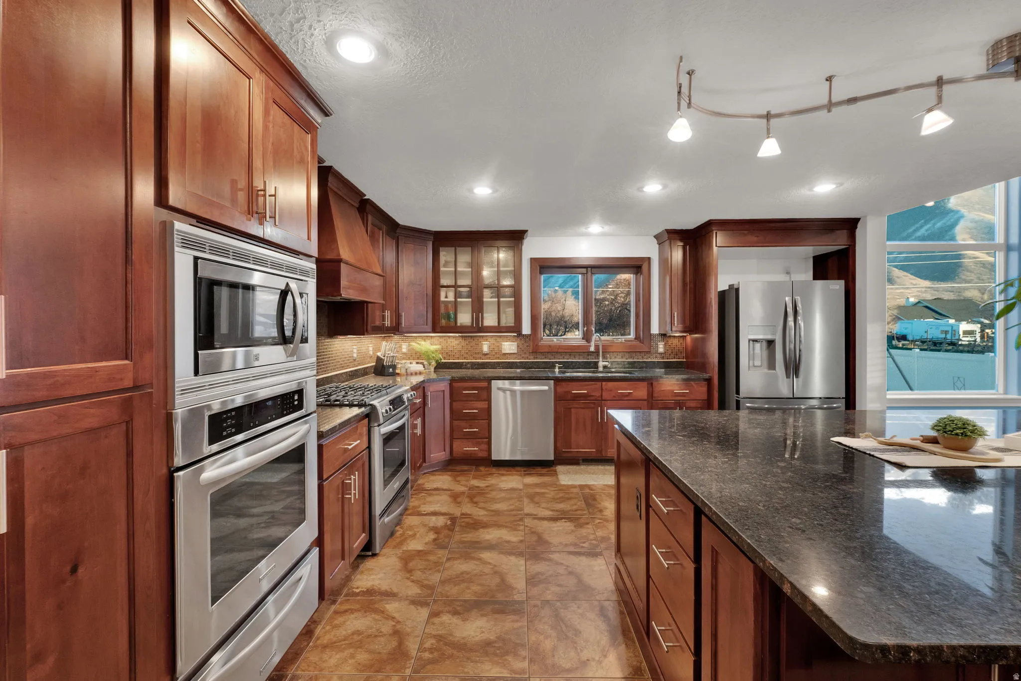 Kitchen with appliances with stainless steel finishes, dark stone countertops, decorative backsplash, a warming drawer, and glass insert cabinets