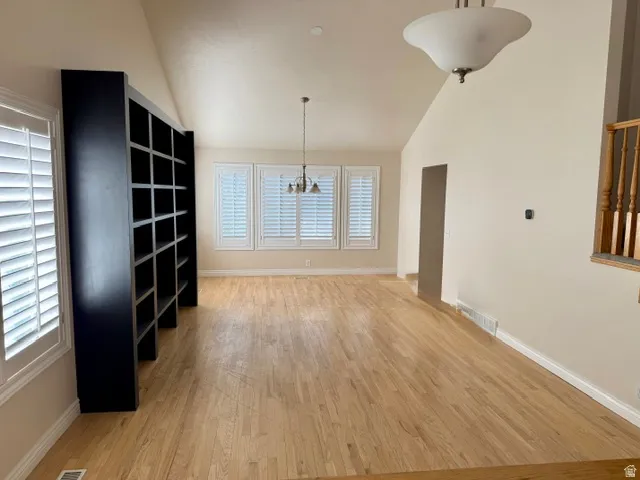 Spacious open room featuring warm wood-finish flooring, vaulted ceilings with recessed lighting, and abundant natural light from multi-panel shuttered windows