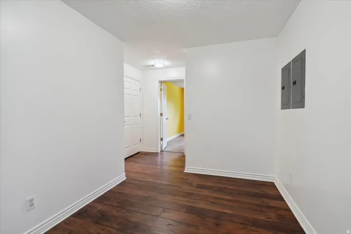 Basement corridor featuring a textured ceiling, dark wood-style flooring, and electric panel