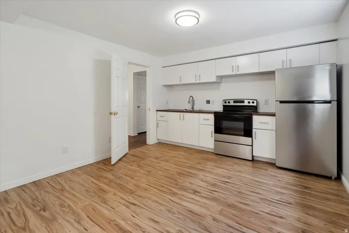 Kitchen with appliances with stainless steel finishes, white cabinetry, light wood-style flooring, and dark countertops