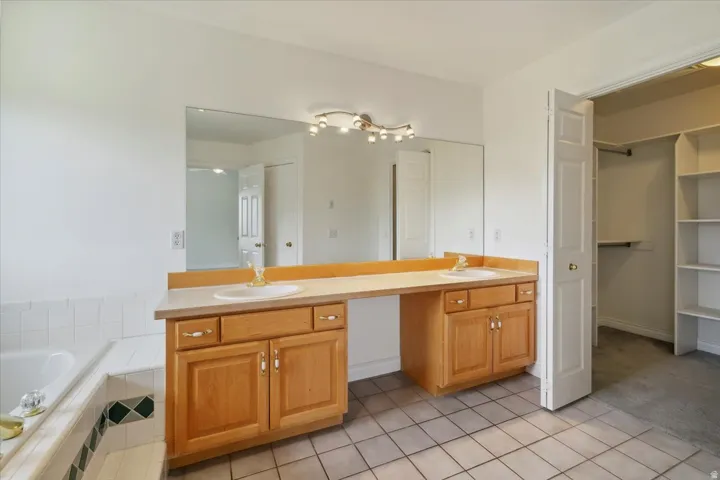 Bathroom with double vanity, a bath, light tile patterned floors, and a walk in closet