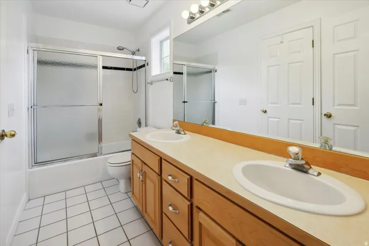 Full bathroom with double vanity, shower / bath combination with glass door, and light tile patterned flooring