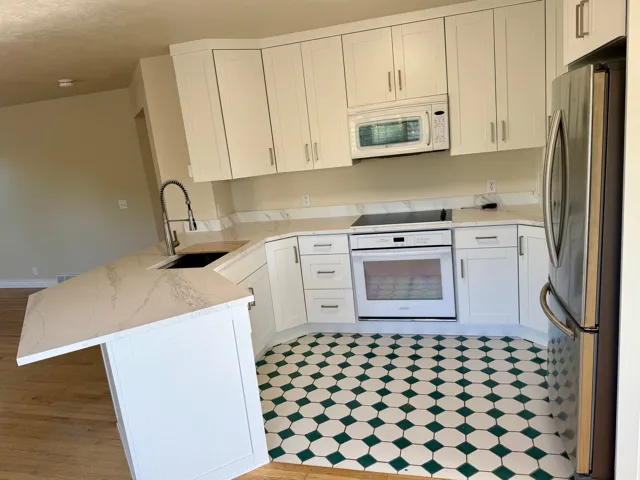 Kitchen featuring white shaker cabinetry, light-toned countertops with a subtle veining pattern, a stainless steel refrigerator, and an integrated oven with a smooth cooktop