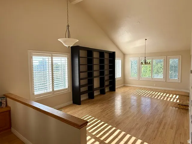 Vaulted ceilings with a built-in bookshelf, wood-finish flooring, and multiple windows with plantation shutters