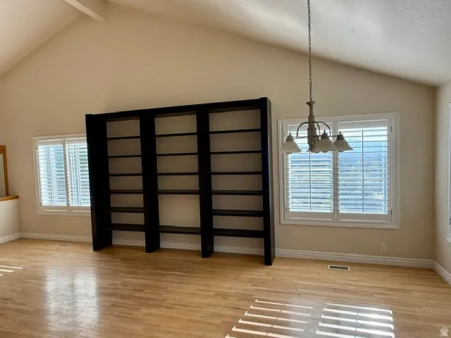 Spacious room with vaulted ceilings, wood-finish flooring, and abundant natural light from multiple shuttered windows