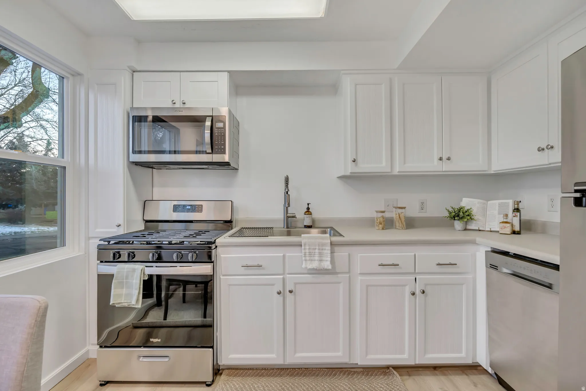 Kitchen featuring stainless steel appliances, white cabinetry, light countertops, and light wood-style flooring