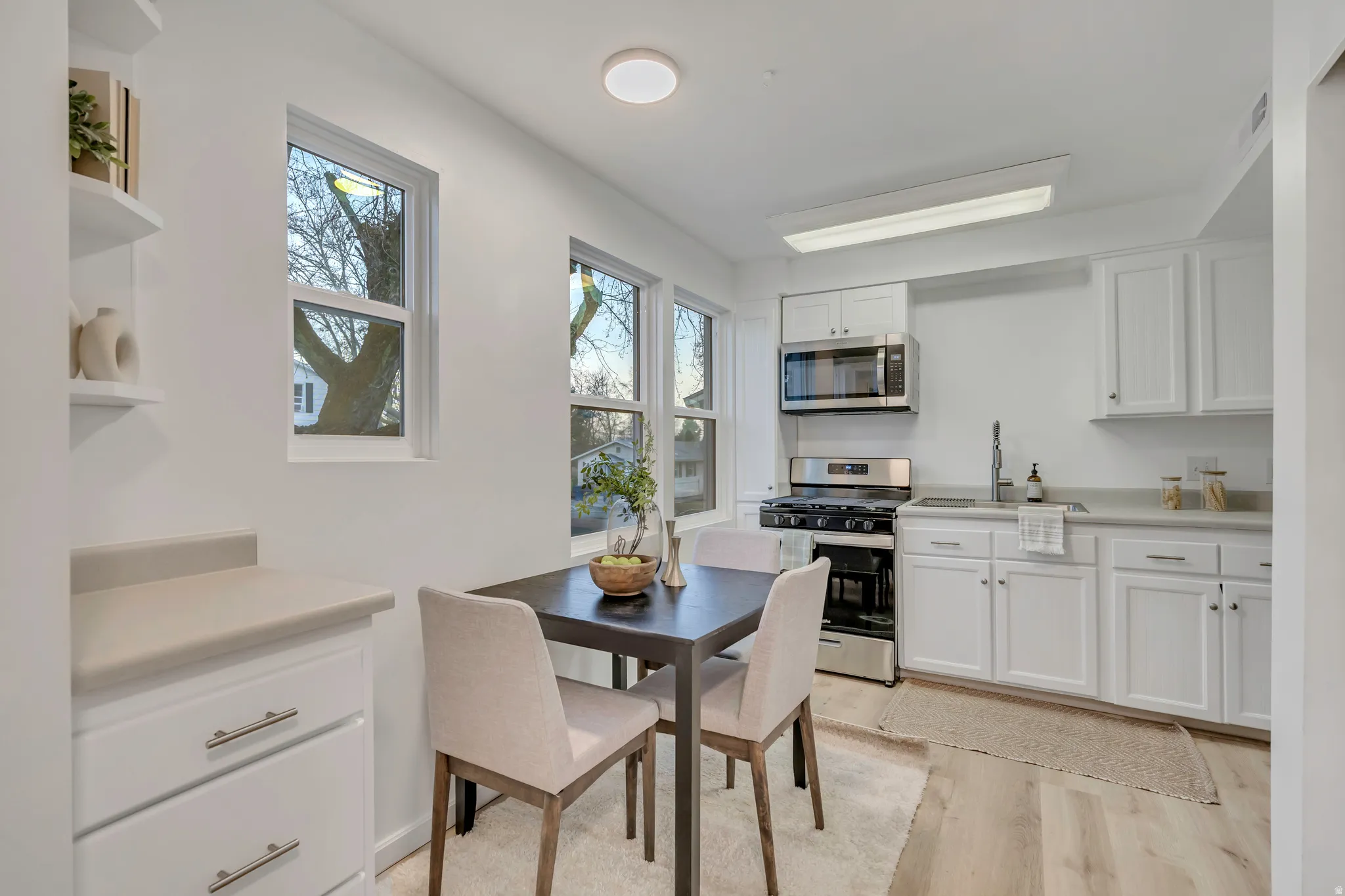 Kitchen featuring white cabinets, open shelves, light countertops, stainless steel appliances, and light wood-style flooring