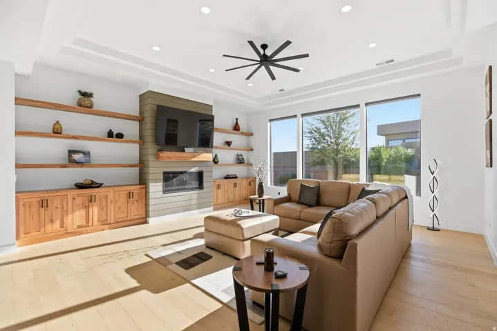 Living room featuring light wood-style flooring, a large fireplace, ceiling fan, recessed lighting, and a raised ceiling
