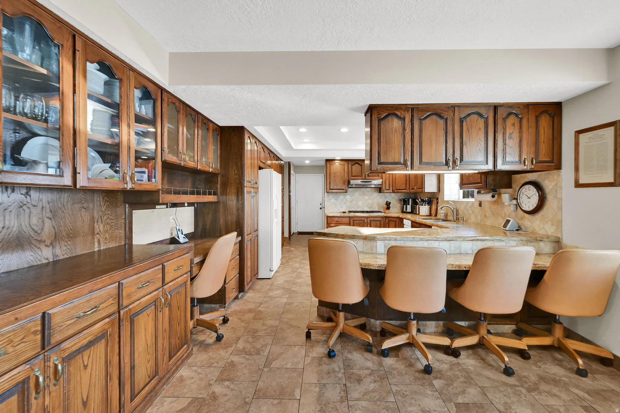 View From Family/Living .Kitchen with built in desk, brown cabinets, a peninsula, glass insert cabinets, and a breakfast bar area