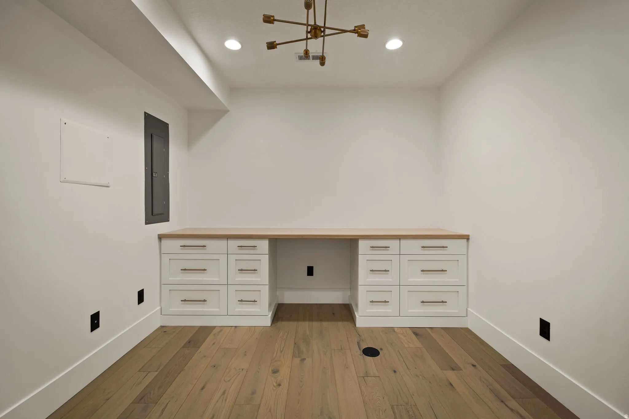 Unfurnished office with built in desk, dark wood-style floors, electric panel, and recessed lighting