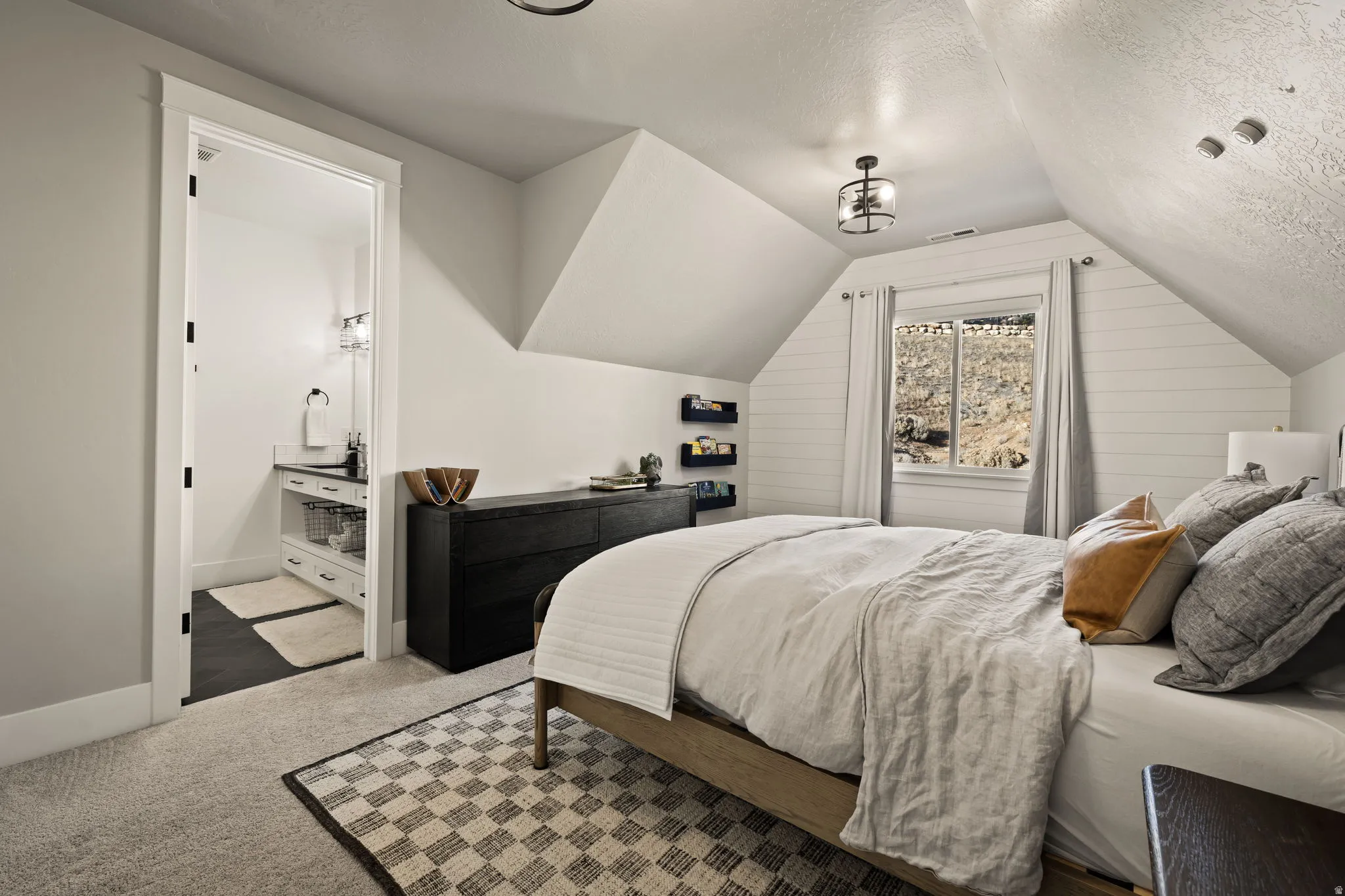 Carpeted bedroom featuring a textured ceiling, lofted ceiling, and ensuite bath