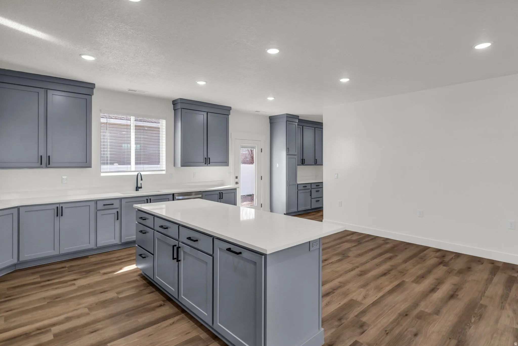 Kitchen featuring gray cabinets, dark wood-style flooring, recessed lighting, a center island, and light stone counters