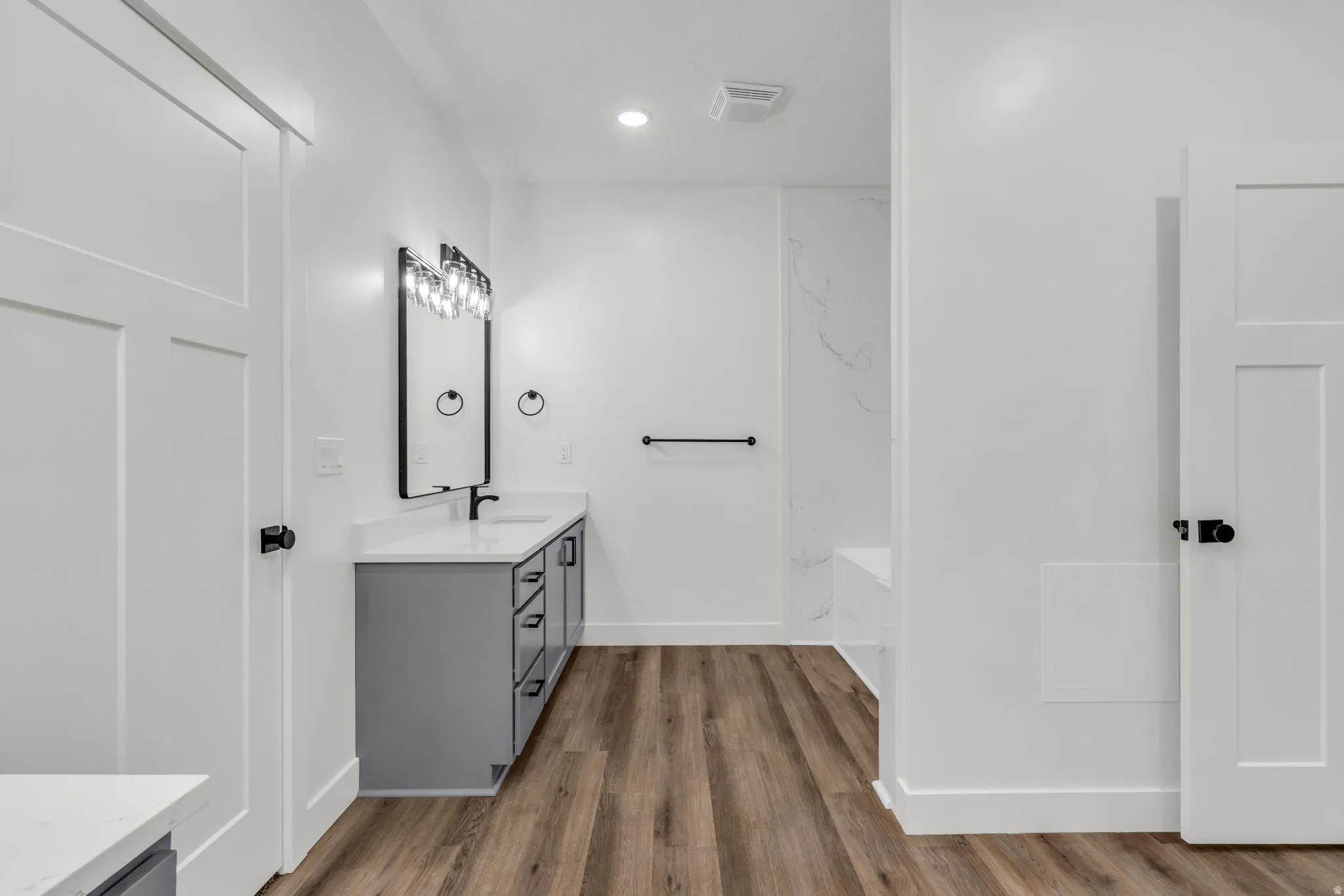 Full bathroom with double vanity, dark wood-style floors, recessed lighting, and a bathtub