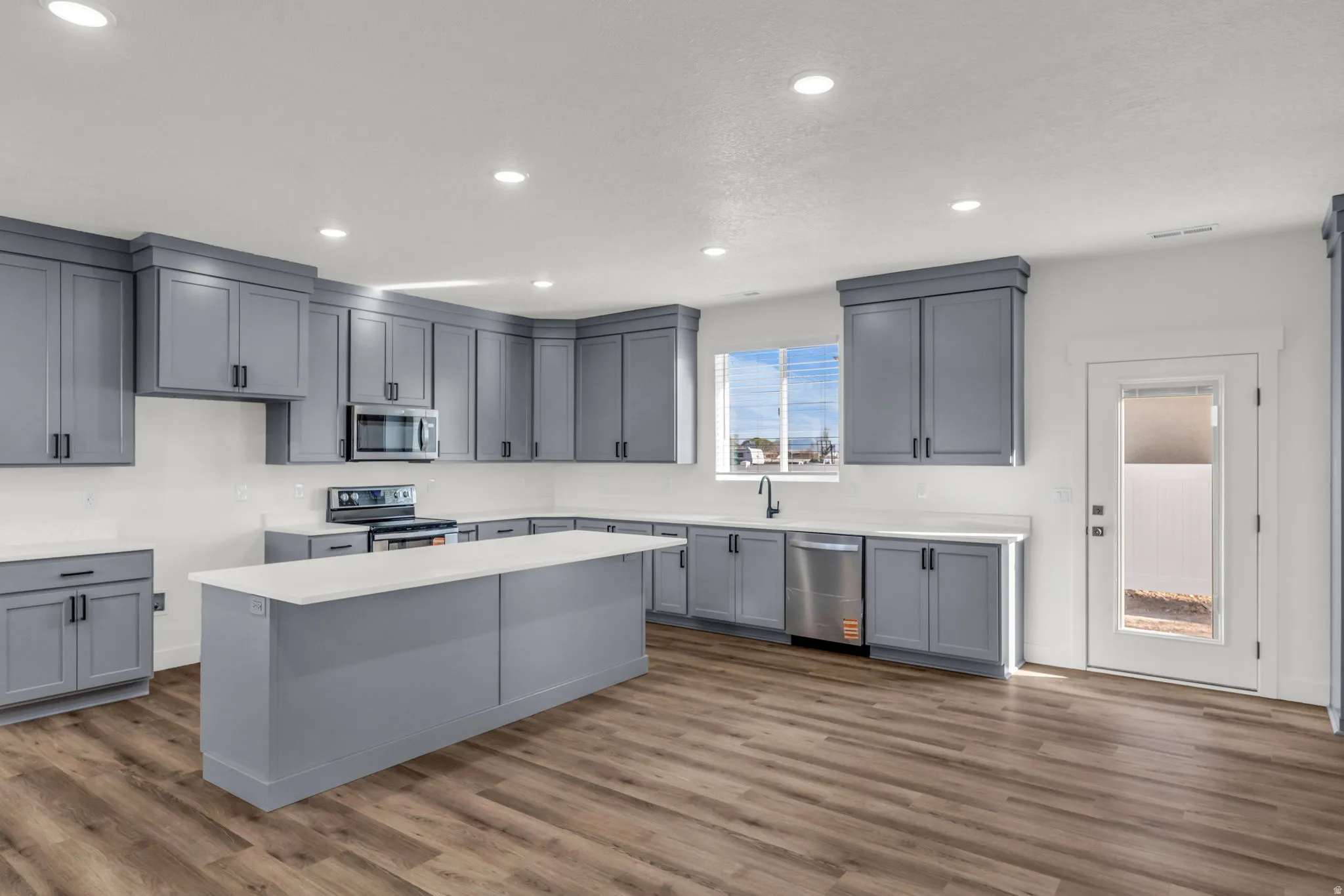 Kitchen featuring gray cabinets, stainless steel appliances, a center island, recessed lighting, and dark wood-style flooring