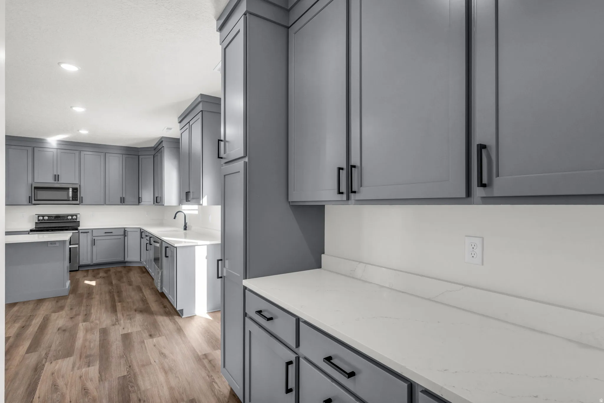 Kitchen featuring gray cabinetry, stainless steel appliances, light wood finished floors, light stone counters, and recessed lighting