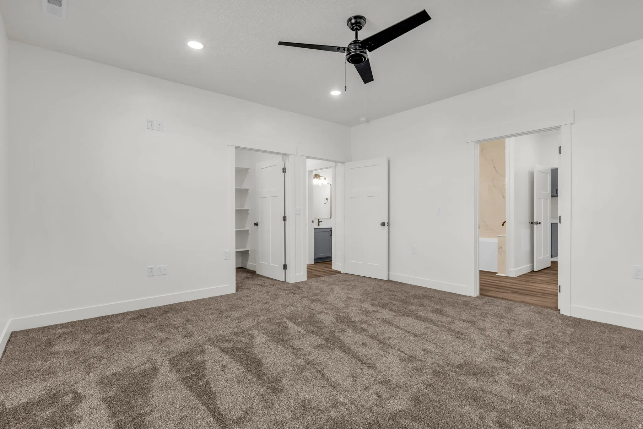 Unfurnished bedroom with a walk in closet, dark colored carpet, a ceiling fan, and recessed lighting