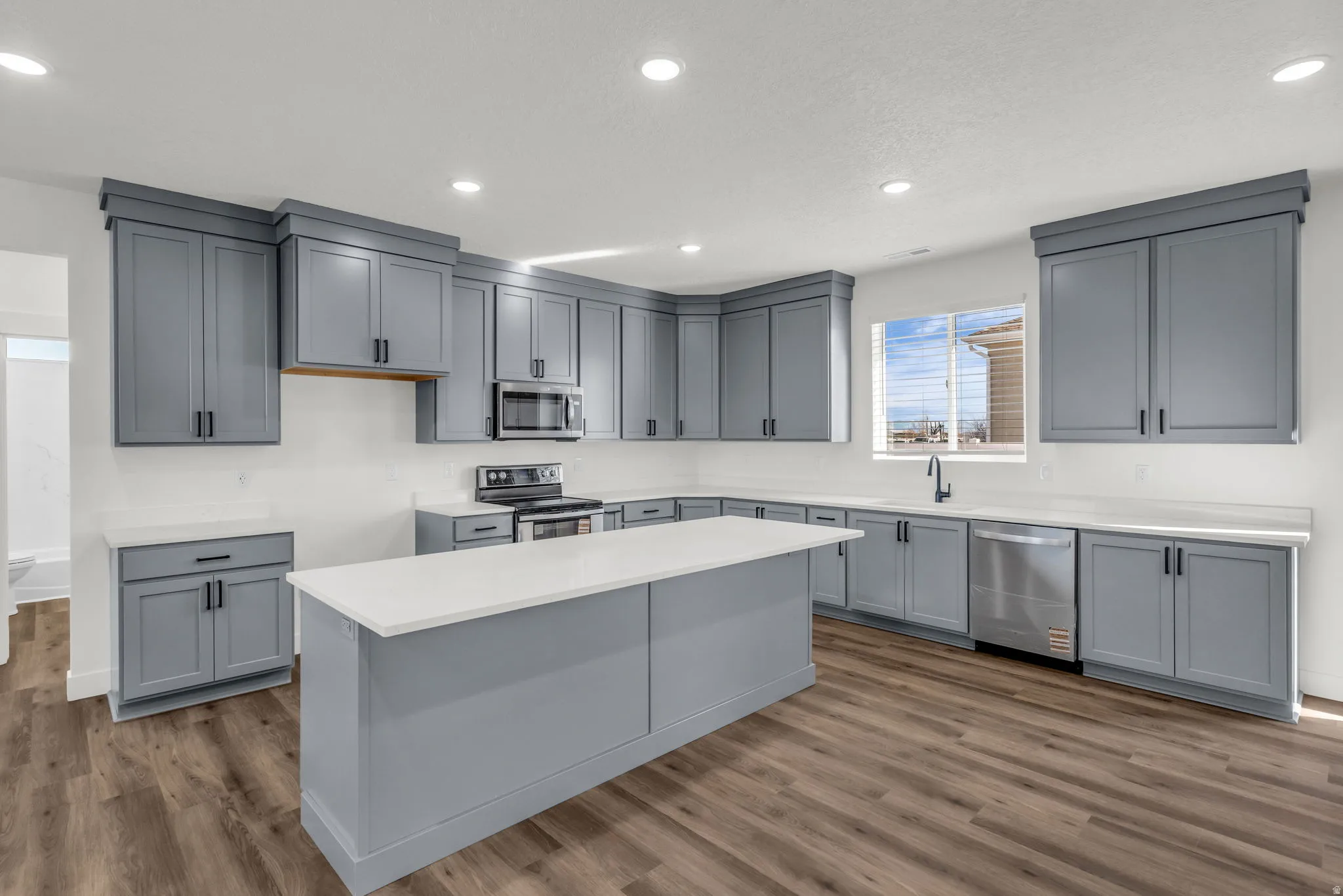 Kitchen featuring gray cabinetry, stainless steel appliances, a center island, dark wood-type flooring, and recessed lighting