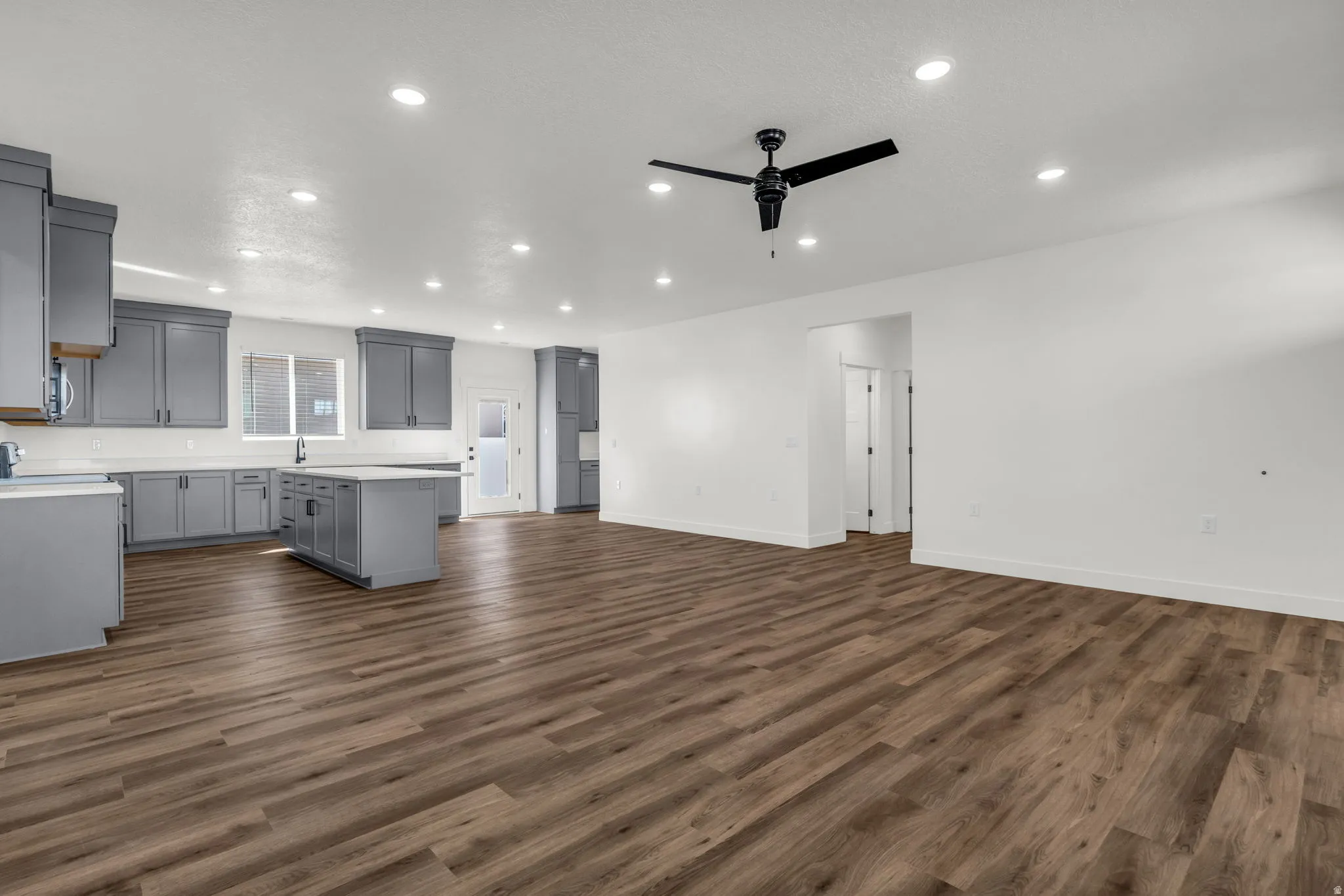 Kitchen featuring gray cabinets, a center island, open floor plan, a ceiling fan, and dark wood-type flooring