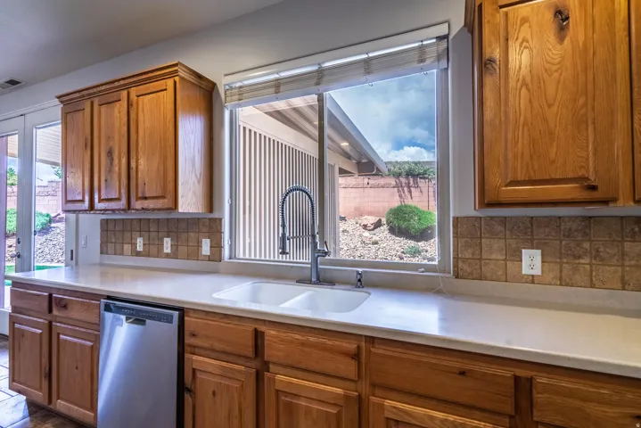 Kitchen featuring brown cabinets, stainless steel dishwasher, decorative backsplash, and plenty of natural light