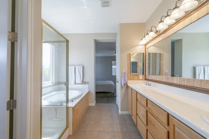 Ensuite bathroom with double vanity, light tile patterned flooring, a bath, a ceiling fan, and a shower stall