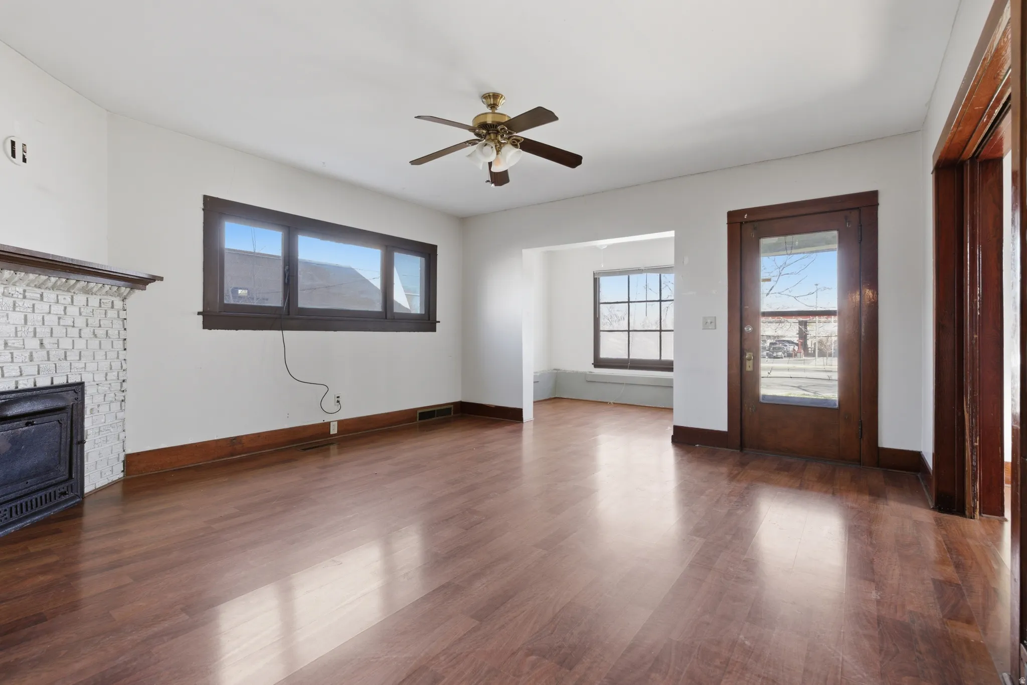 Unfurnished living room with dark wood-type flooring, a ceiling fan, and a brick fireplace