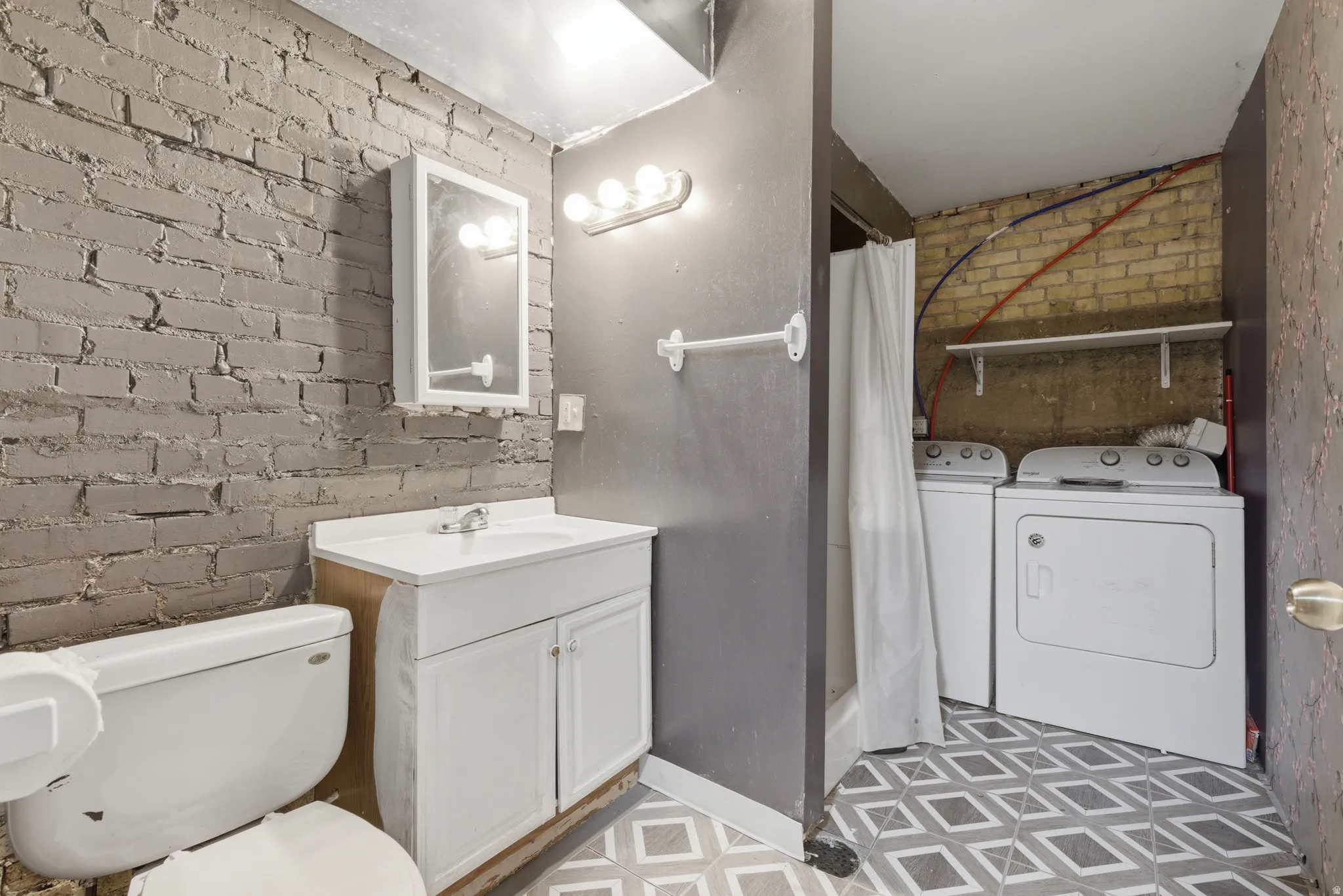 Full bathroom featuring brick wall, a shower with shower curtain, vanity, independent washer and dryer, and light flooring