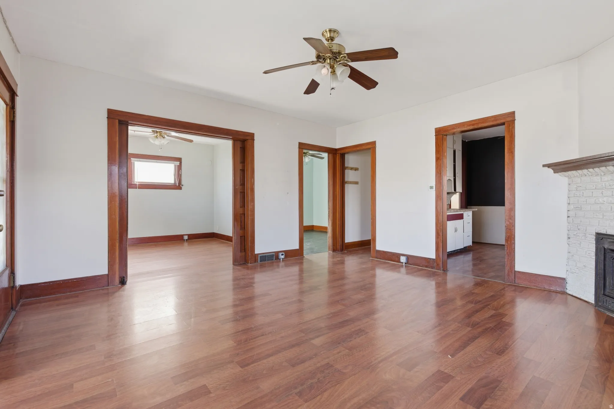Unfurnished living room with dark wood-style floors, ceiling fan, and a brick fireplace