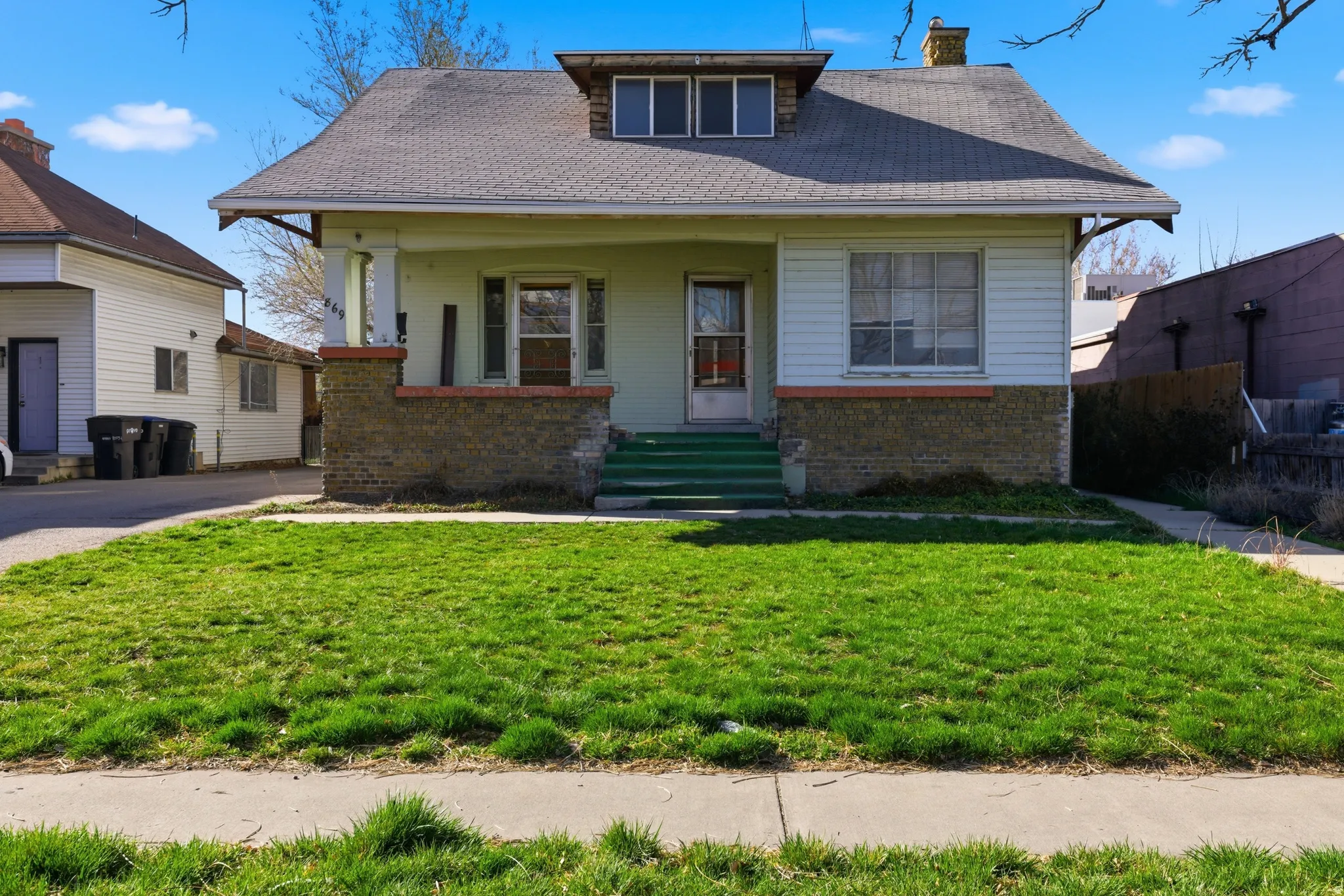 Bungalow featuring brick siding, covered porch, a front lawn, a chimney, and roof with shingles