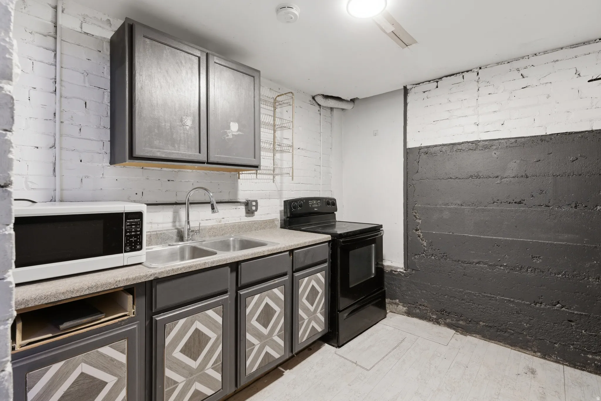 Kitchen featuring black electric range oven, gray cabinetry, white microwave, and light countertops