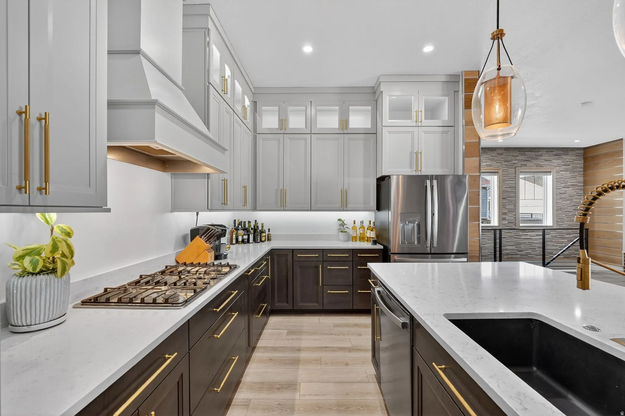 Kitchen featuring two tone cabinets with upgraded hardware, granite countertops, decorative light fixtures, included appliances with stainless steel finishes, recessed lighting, and custom range hood, gas stove and water fall extended island