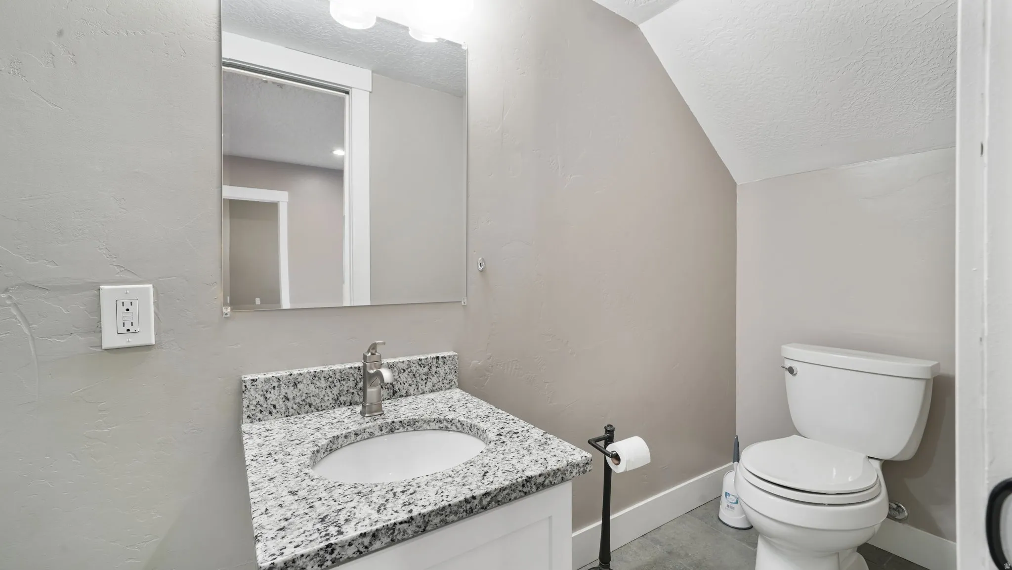 Bathroom with a textured wall, a textured ceiling, vanity, and vaulted ceiling