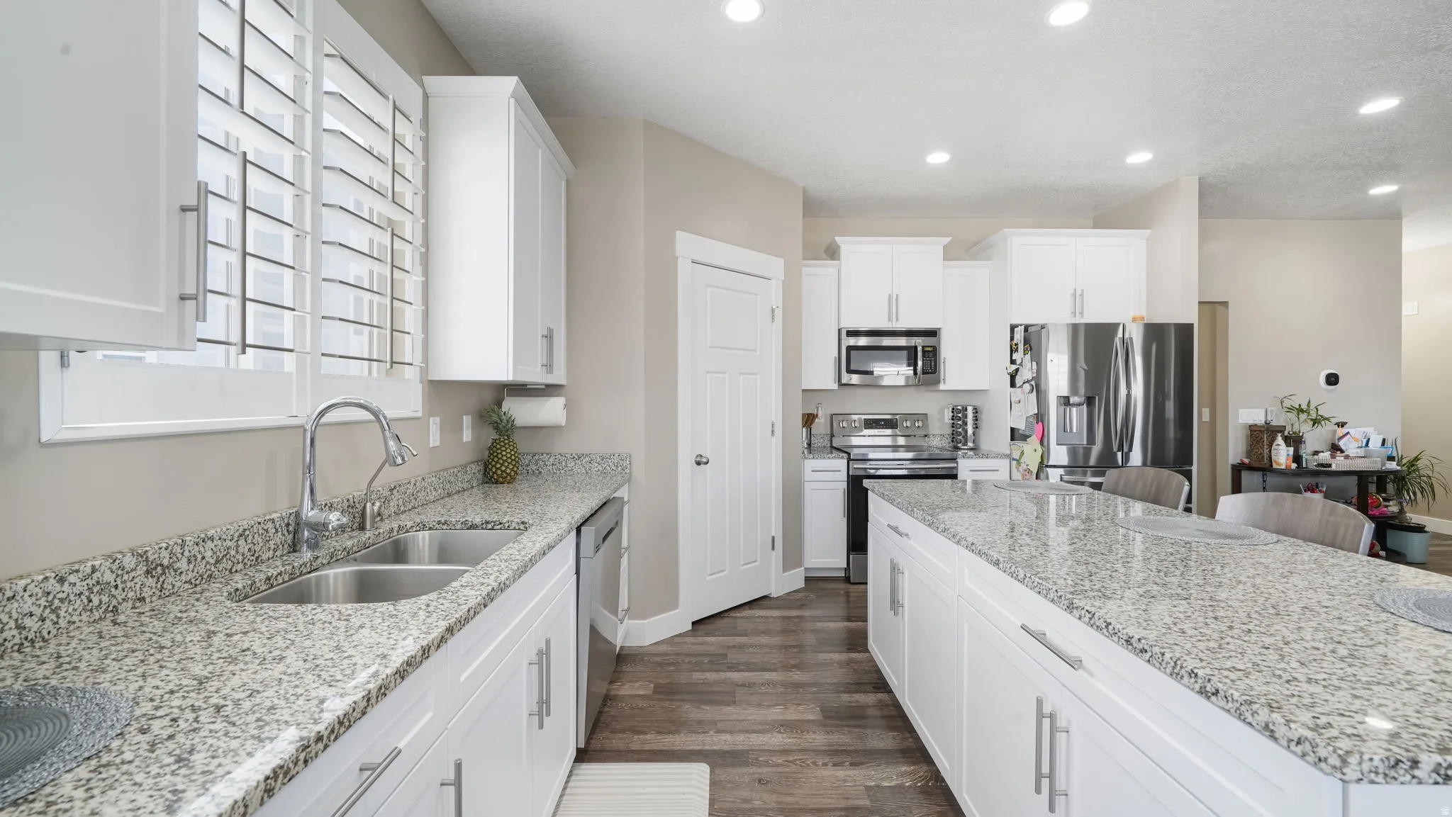 Kitchen with white cabinets, appliances with stainless steel finishes, light stone countertops, dark wood-style flooring, and recessed lighting