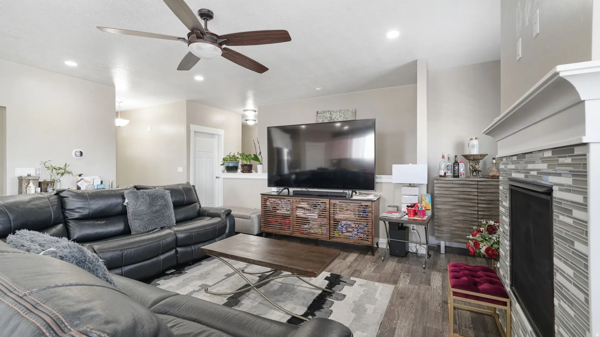 Living room with wood finished floors, a ceiling fan, a fireplace, and recessed lighting