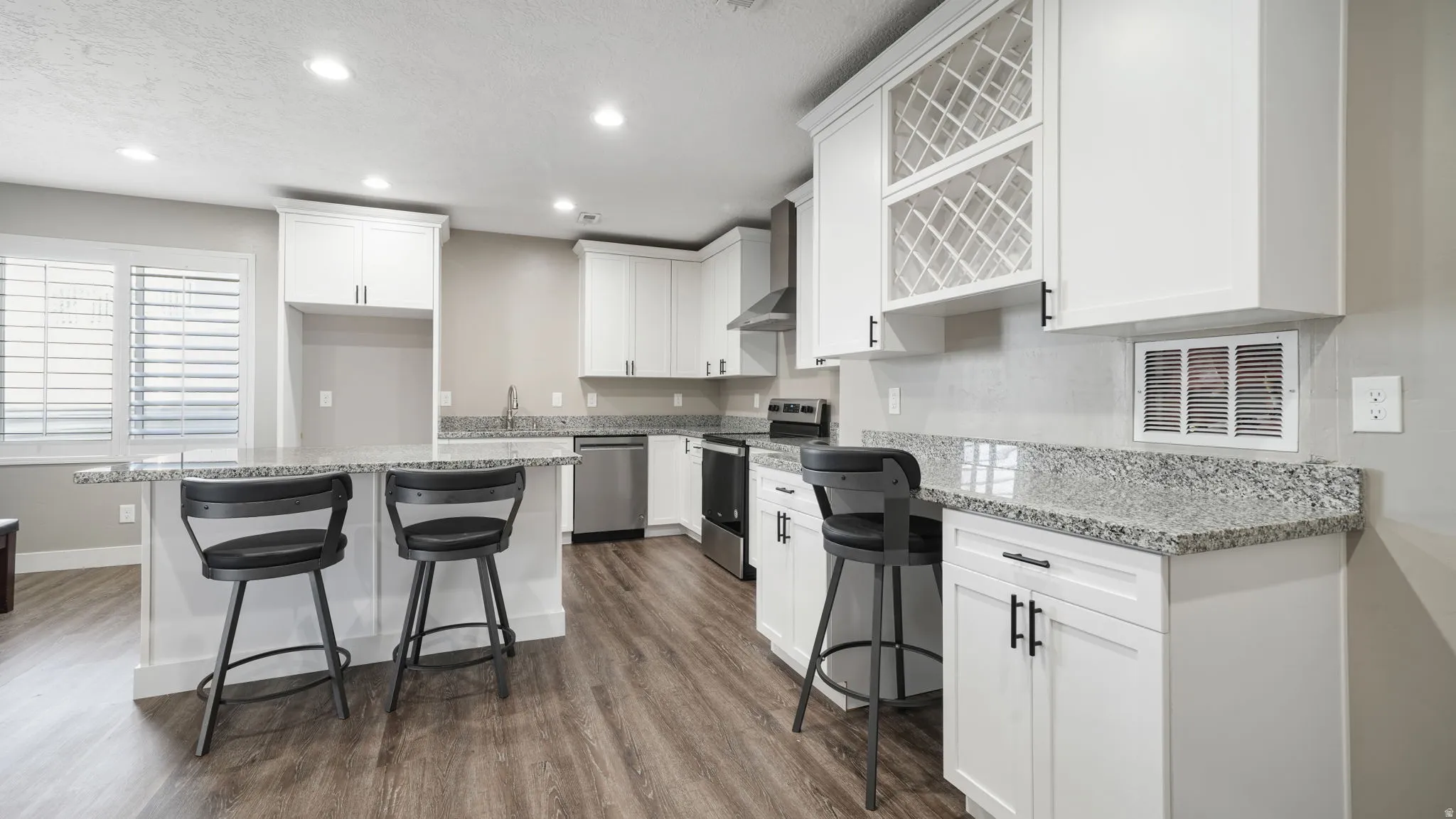 Kitchen with stainless steel appliances, recessed lighting, white cabinets, a kitchen bar, and light stone countertops