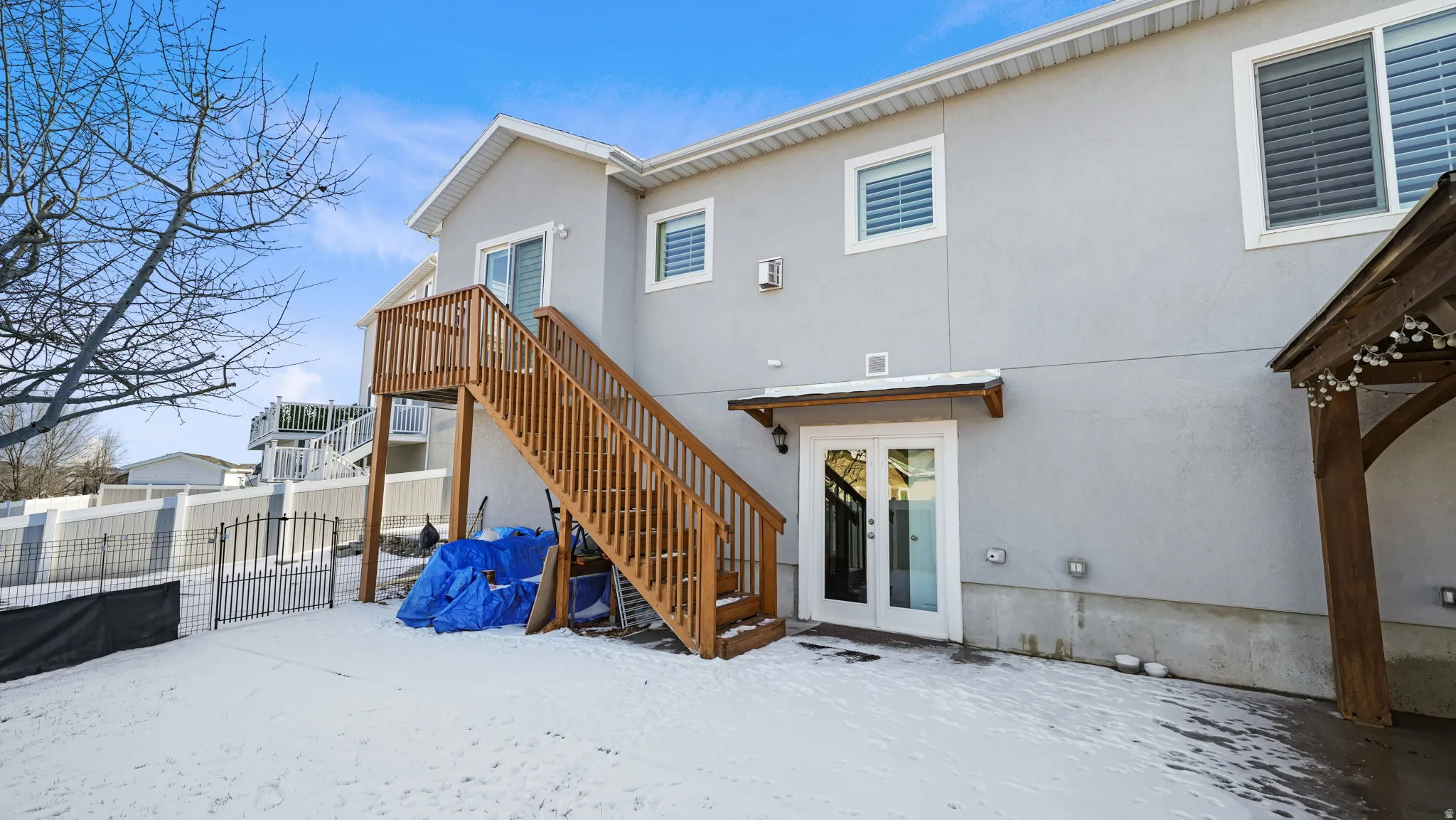 Snow covered house with a gate, stairway, and stucco siding