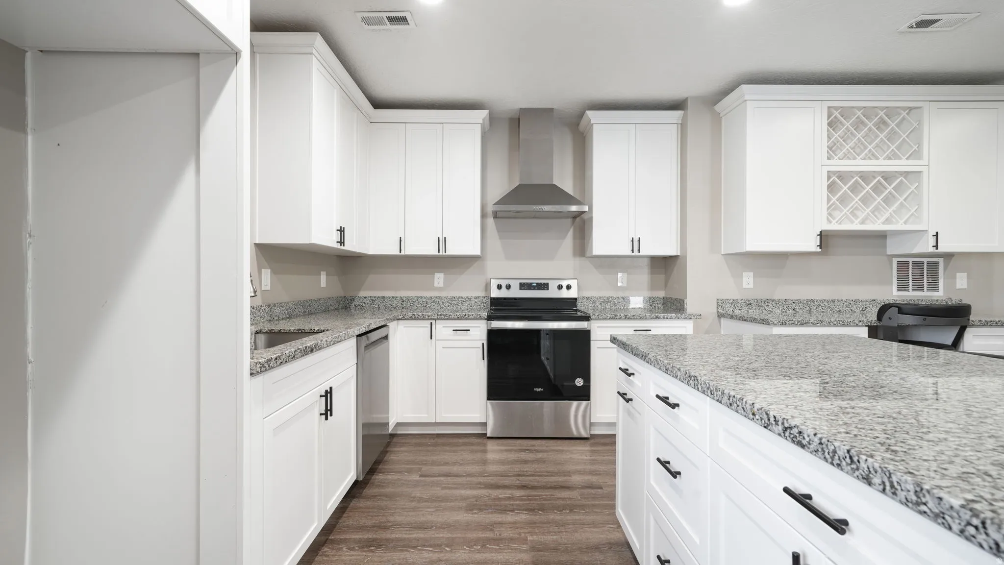 Kitchen featuring appliances with stainless steel finishes, white cabinetry, wall chimney range hood, light stone counters, and dark wood-type flooring