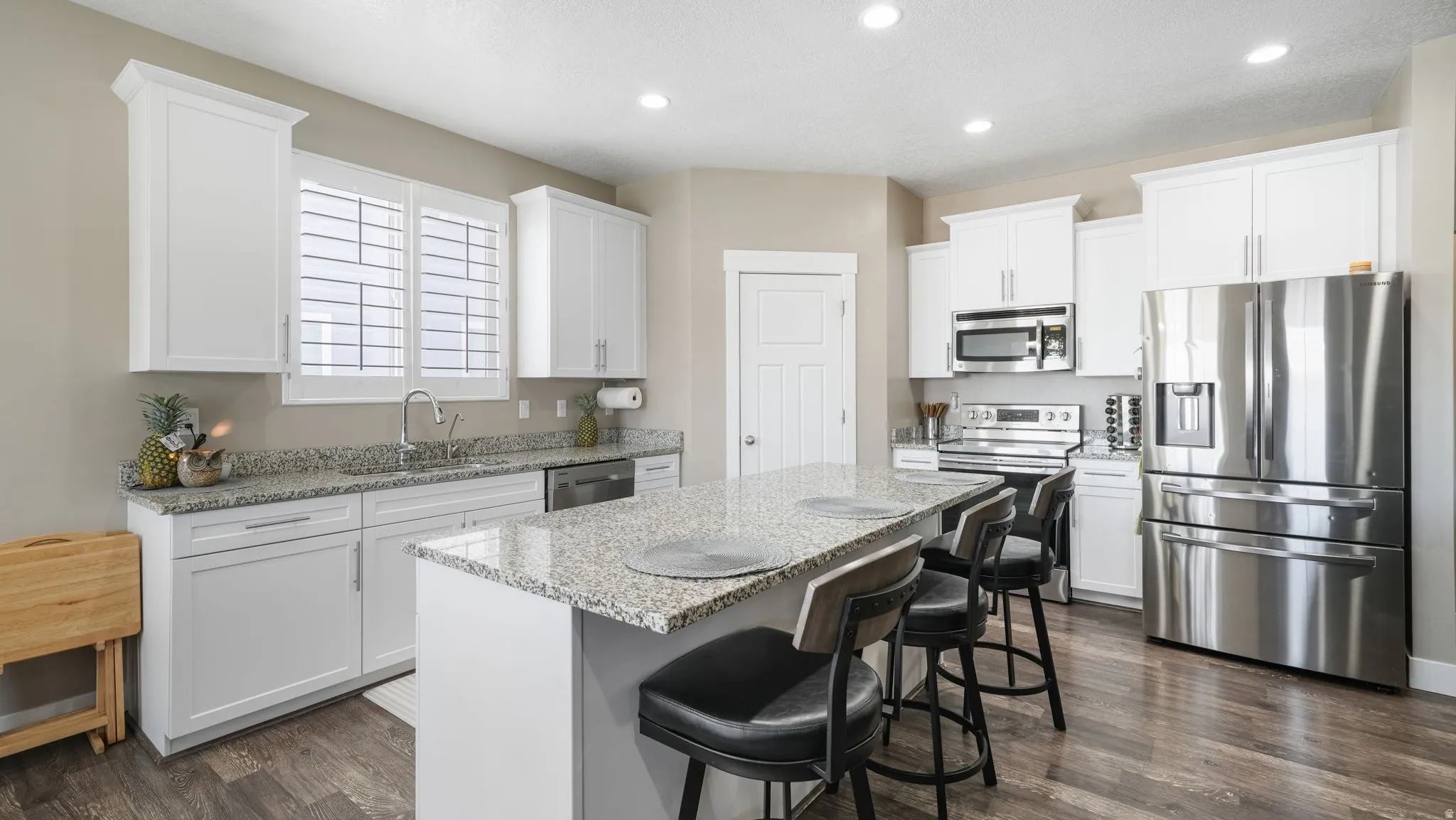 Kitchen with stainless steel appliances, light stone countertops, white cabinetry, a center island, and a breakfast bar area