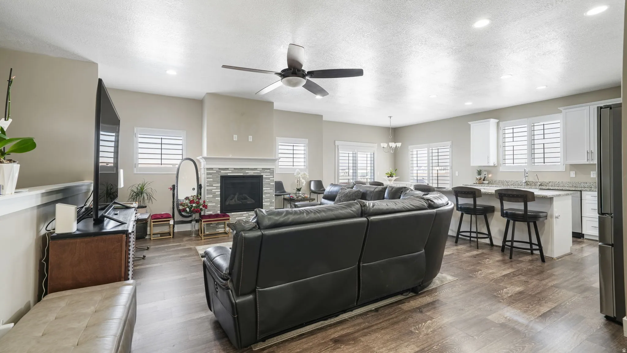 Living room featuring a textured ceiling, ceiling fan, a chandelier, recessed lighting, and dark wood-type flooring