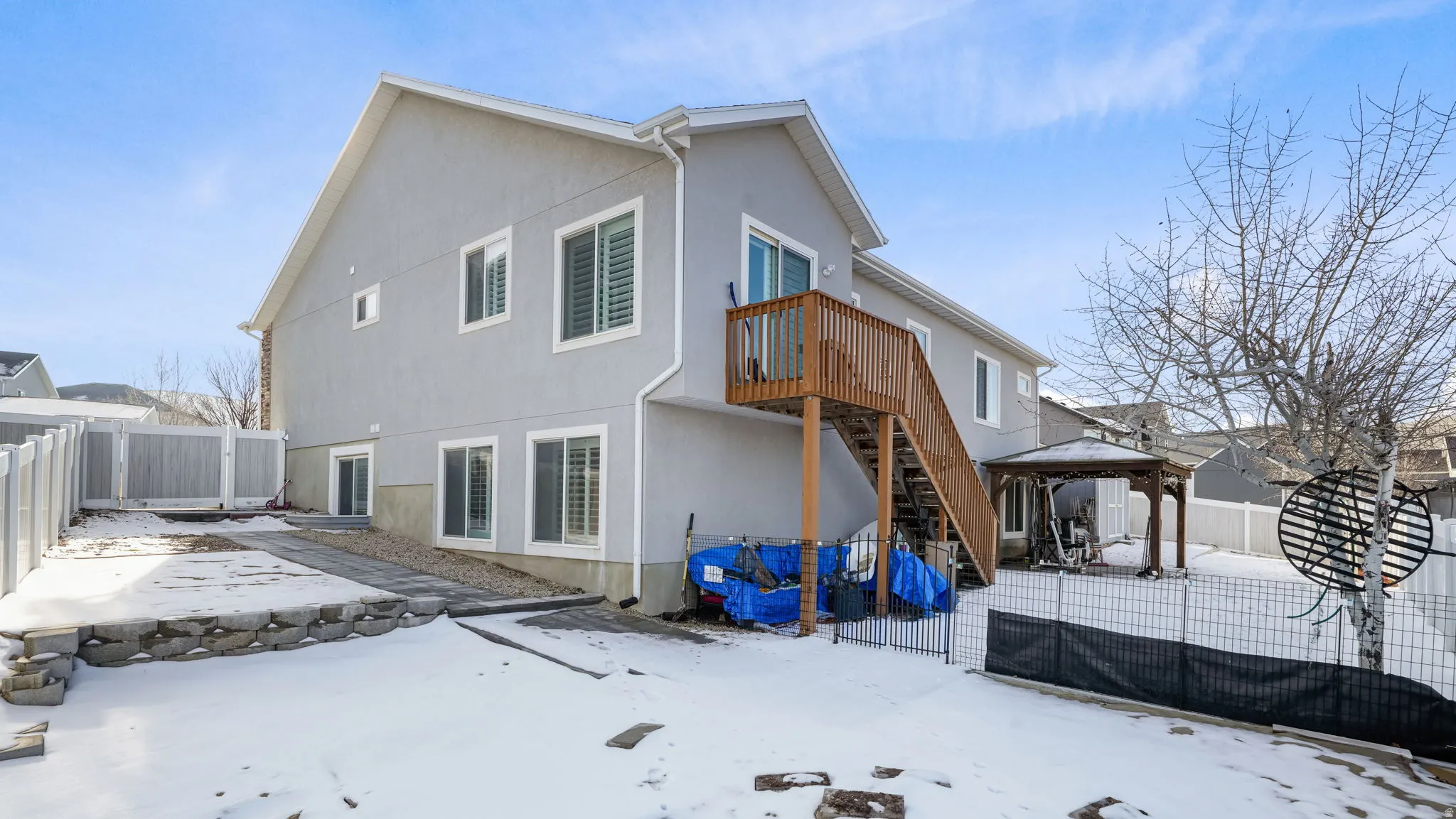 Snow covered rear of property with a patio, a fenced backyard, stucco siding, a gazebo, and stairs