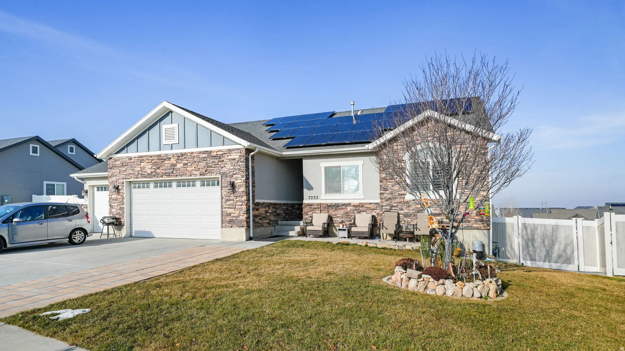View of front of property with concrete driveway, board and batten siding, stone siding, roof mounted solar panels, and an attached garage