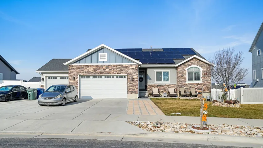 View of front facade featuring board and batten siding, roof mounted solar panels, driveway, and an attached garage