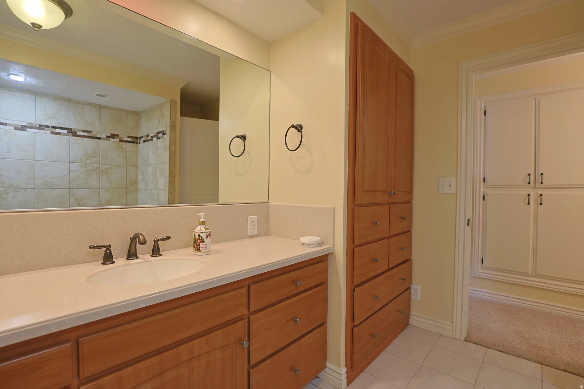 Bathroom with ornamental molding, vanity, light tile patterned floors, and a tile shower