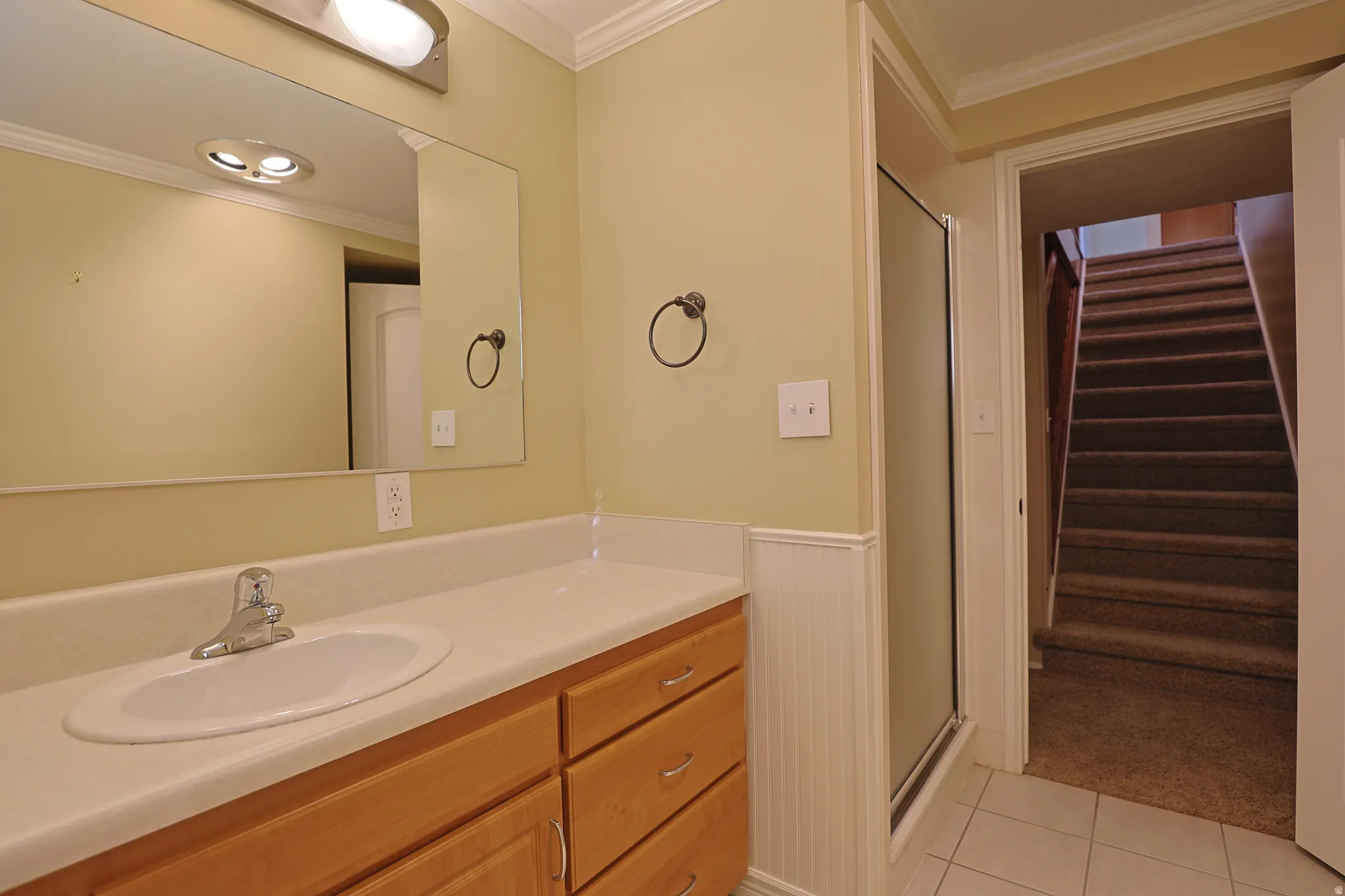 Bathroom featuring crown molding, vanity, light tile patterned floors, a stall shower, and wainscoting