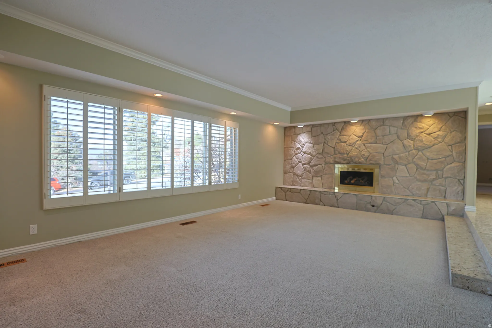 Unfurnished living room with a fireplace, carpet flooring, and ornamental molding