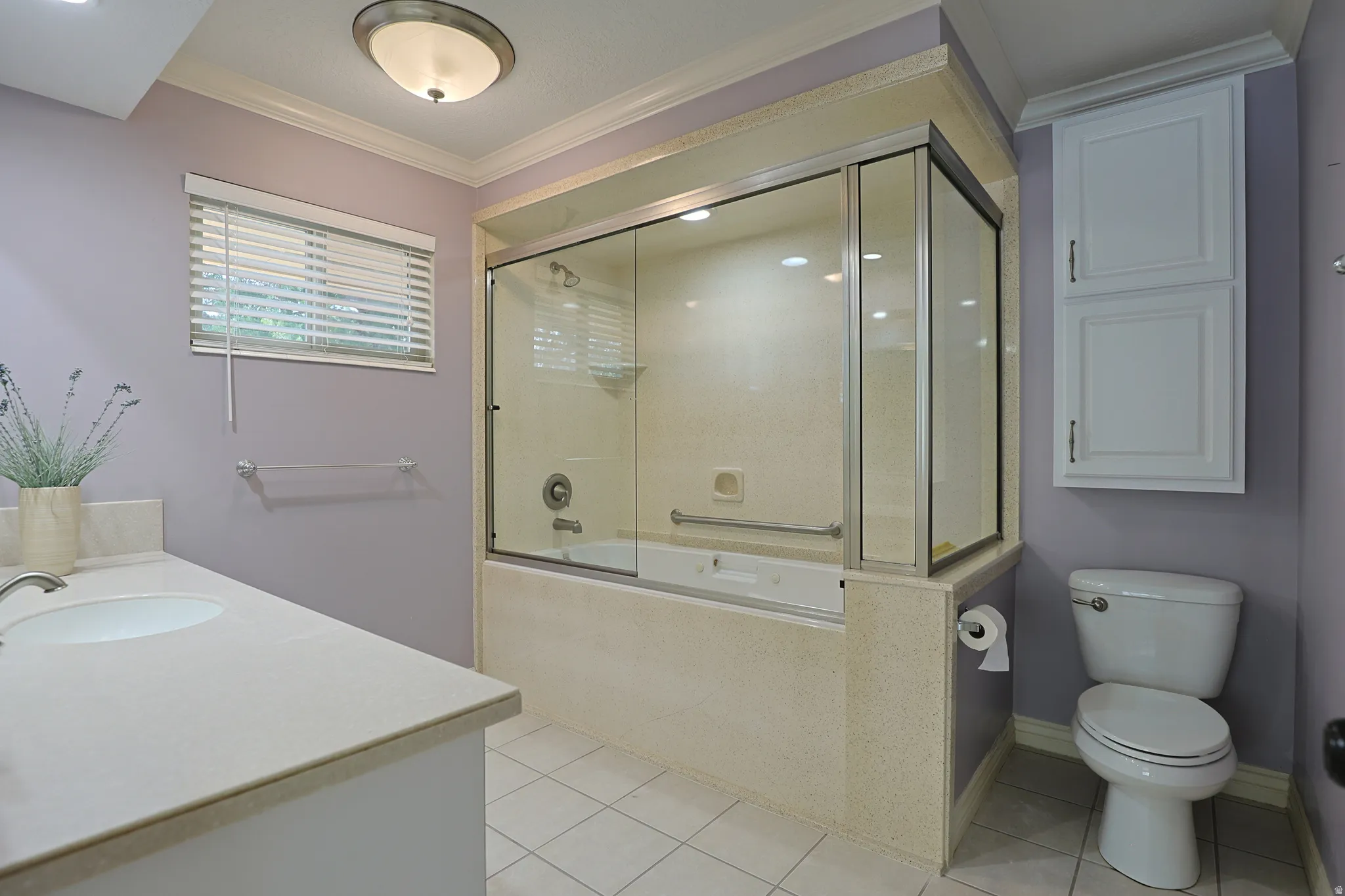 Full bath featuring vanity, light tile patterned floors, crown molding, and shower / bath combination with glass door