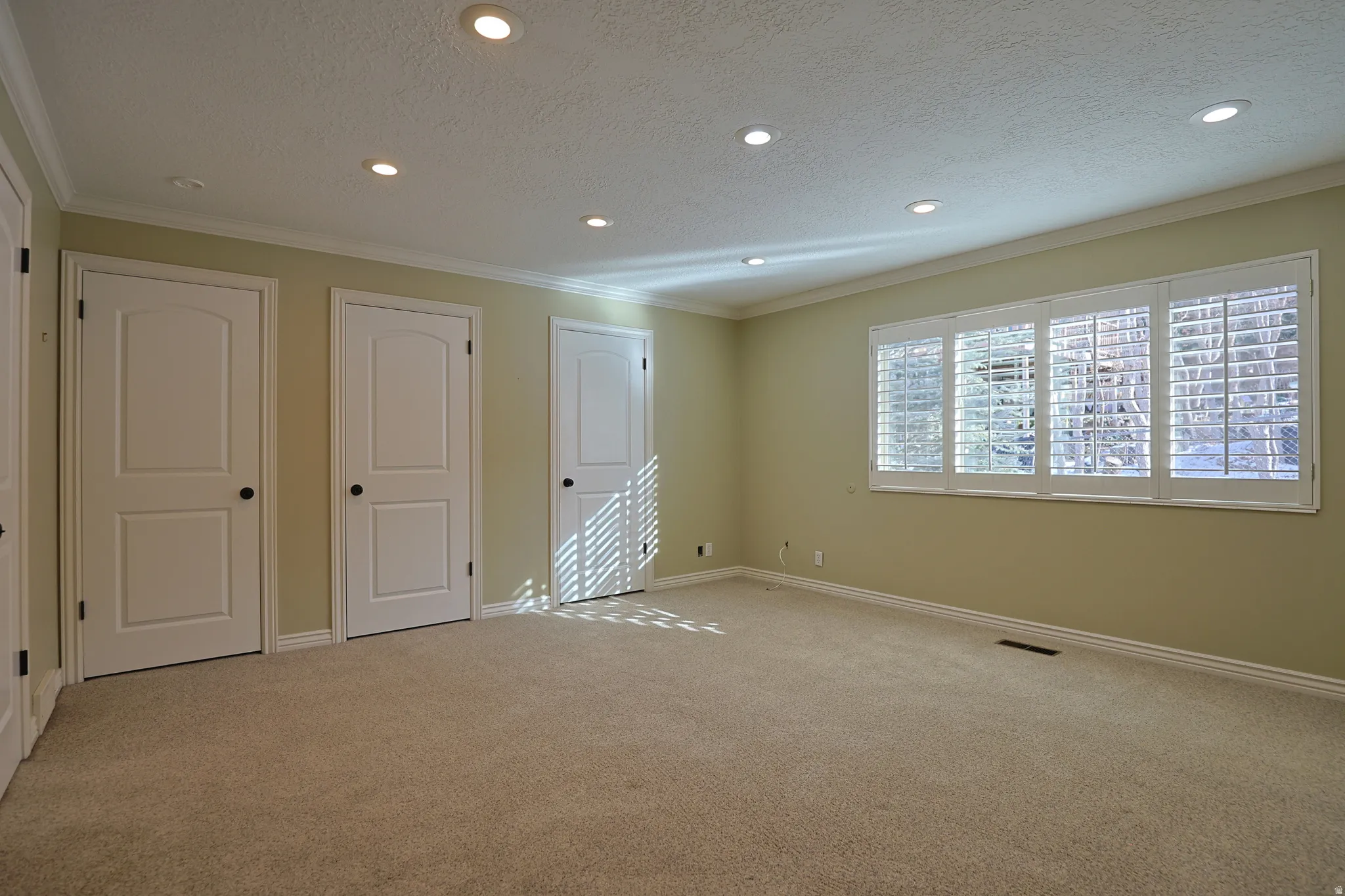 Unfurnished bedroom featuring a textured ceiling, ornamental molding, carpet flooring, recessed lighting, and multiple closets