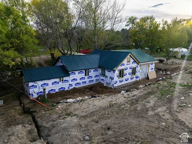 New construction framed structure with a green metal roof, multiple windows, and a partially excavated site