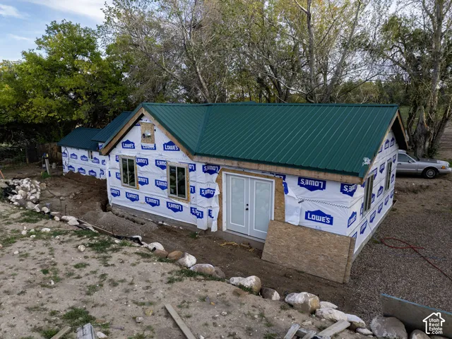 Structure under construction featuring a green metal roof, multiple windows, and a set of white double doors